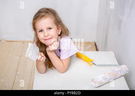 Repair in the apartment. Happy family mother and little daughter in blue aprons paints the wall with white paint. The girl took a break and smiles Stock Photo