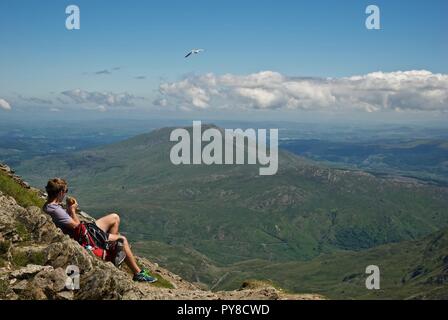 A male walker enjoys the view at the summit of Mount Snowdon, Snowdonia National Park, Gwynedd, North Wales, UK Stock Photo
