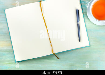 An overhead photo of an open journal notebook with a pen and a cup of tea, shot from the top, a diary on a teal blue background with copy space Stock Photo
