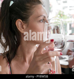 Young woman with a natural make - up and a  ponytail holding a red wine glass. Defocused blurry background. Stock Photo
