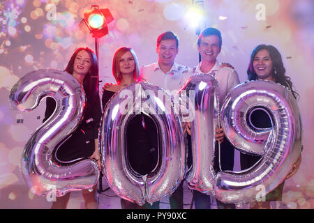 New Year party concept. Group of young friends holding silver colored numbers 2019 and throwing confetti Stock Photo