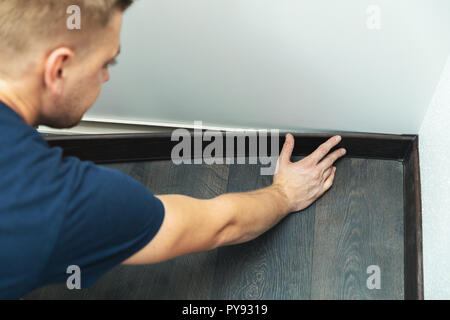 worker installing plastic baseboard on the laminate floor Stock Photo