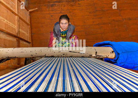 Local girl weaving rug and looking up the weaving loom, in Nukus, Uzbekistan Stock Photo