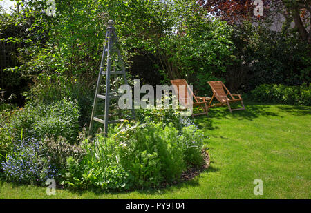 Summer boarder with wooden obelisk plant support feature and wooden garden chairs in English Garden,England,Europe Stock Photo