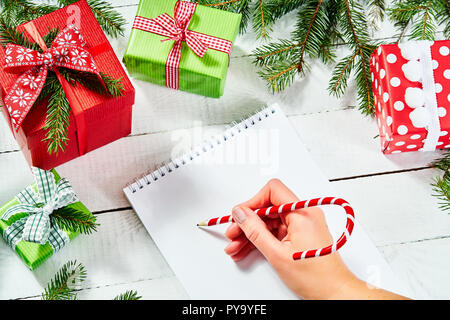 hand of a woman writing a letter to santa on an old white wooden table with christmas decorations Stock Photo
