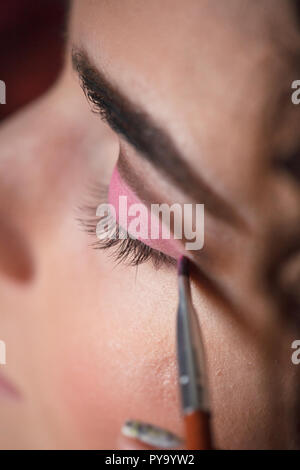 Eyeshadow applying, makeup for eyes closeup. Young woman applies pink colored eyeshadow with make up brush. Stock Photo