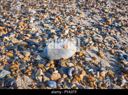 Close up of a large pebble with a small pebble on top surrounded by more small pebbles on a beach with sand underneath Stock Photo