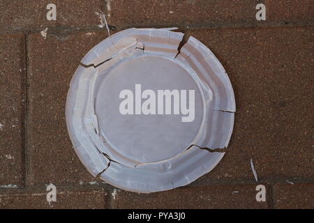 Crushed Disposable Plate. Disposable plate squeezed on the sidewalk. Disposable dish cracked on the pavement, top view. Used disposable tableware. Stock Photo