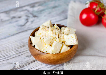 Feta cheese cubes in wooden plate on white wood Stock Photo