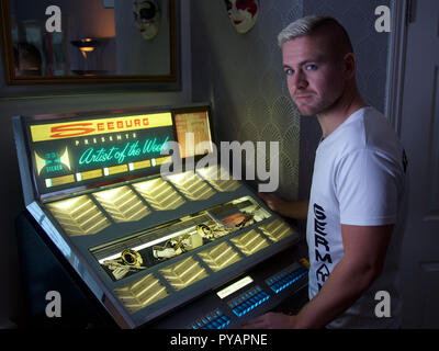 A young man standing by a Seeburg juke box, looking at camera ,  England Stock Photo