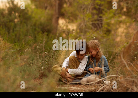 Cute boy and girl touching heads while sitting on ground in majestic countryside Stock Photo