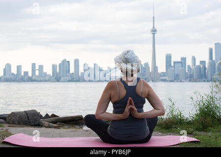 Middle aged woman practicing yoga lotus position at the front of Toronto  from Island over the lake Ontario Stock Photo