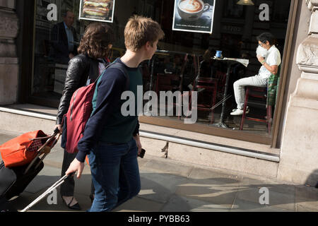 Passers-by look at a man eating his own food from a plastic bag in the sunlit window of a central London cafe, on 25th October 2018, in Piccadilly, London, England. Stock Photo