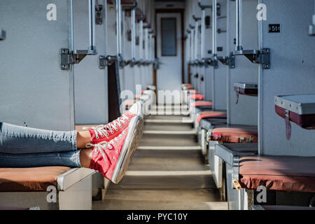 Woman legs in red tennis shoes in a vintage empty train car. Female in canvas shoes rests on seats of an old soviet economy class carriage Stock Photo