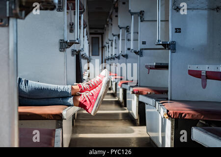 Woman legs in red tennis shoes in a vintage empty train car. Female in canvas shoes rests on seats of an old soviet economy class carriage Stock Photo