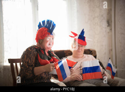 Pastimes. An elderly women supports sport team sitting against TV on the backgrond of window. Portrait Stock Photo