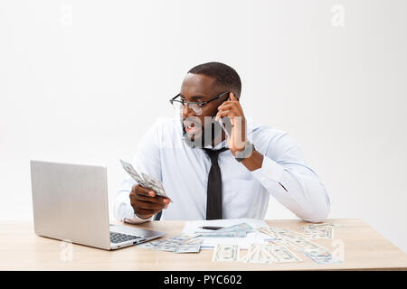 Irritated dark skinned young male enterpreneur being on working place feels very stressed and angry as cannot manage to do all work, surrounded with modern gadgets, looks in displeasure away Stock Photo
