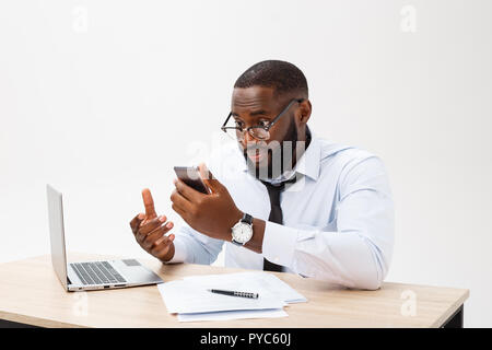 Irritated dark skinned young male enterpreneur being on working place feels very stressed and angry as cannot manage to do all work, surrounded with modern gadgets, looks in displeasure away Stock Photo