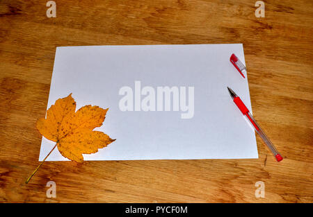 Maple leaf, white sheet of paper with pen on wooden table. Autumn season write letters and send postcards to relatives and friends in faraway countrie Stock Photo