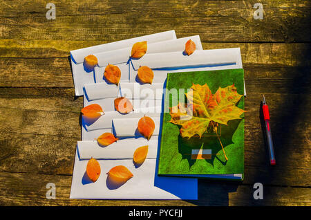 Composition of white postal envelopes for sending letters with yellow autumn leaves, diary-notebook and ink manual on a wooden background lit by the s Stock Photo