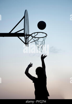 Silhouette of a young girl shooting a basketball Stock Photo