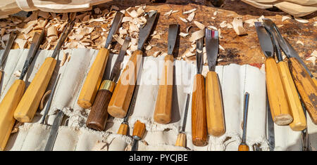 A set of wood carving tools, arranged on a white cloth on a wooden surface,with wood chips scatterd among them Stock Photo