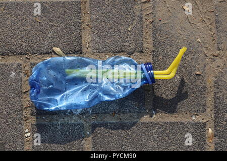 Crushed Plastic Bottle on the Sidewalk. Blue squeezed plastic bottle with two drinking straws inside, on the pavement. Disposable bottle thrown away. Stock Photo