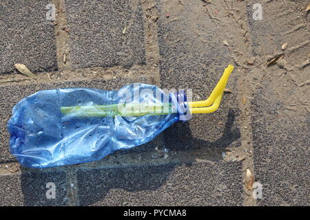 Crushed Plastic Bottle on the Sidewalk. Blue squeezed plastic bottle with two drinking straws inside, on the pavement. Disposable bottle thrown away Stock Photo