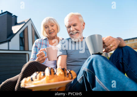 Caring retired husband bringing some biscuits for wife while drinking tea Stock Photo