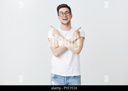 Both ways good. Portrait of happy carefree handsome young european man in glasses with brislte smiling and laughing from joy crossing hands on body pointing sideways at cool choices over copy space Stock Photo