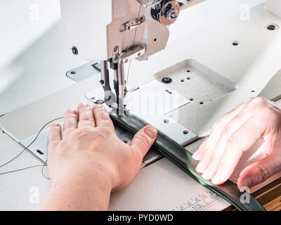 workshop of making textile and leather travel bag - craftsman sews green belt on industrial sewing machine Stock Photo