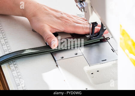 workshop of making textile and leather travel bag - craftsman stitches the belt for a bag on sewing machine Stock Photo