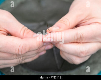 workshop of making the leather bag for jewelry - craftsman inserts thread in needle eye to sew the pouch Stock Photo