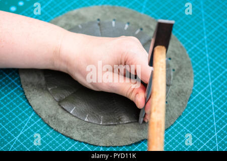 workshop of making the leather bag for jewelry - craftsman makes holes in the stitched pouch by punch Stock Photo