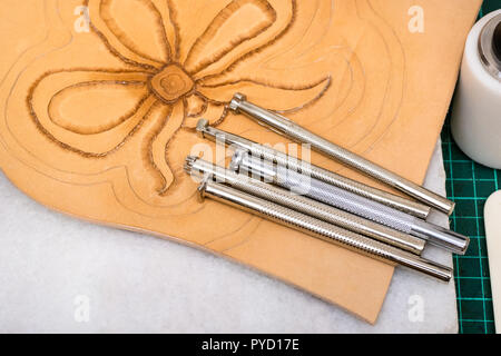 workshop of making the carved leather bag - top view of various Stamping tools on surface of partly carved leather Stock Photo