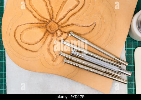 workshop of making the carved leather bag - top view of various Stamping tools on partly carved rough leather Stock Photo