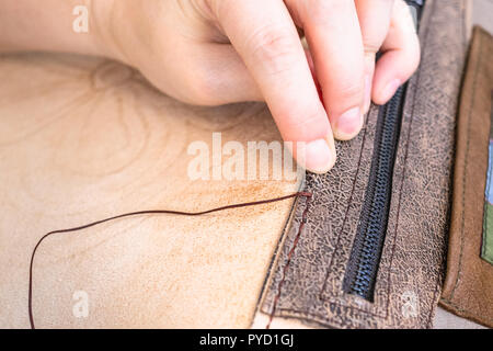 workshop of making the carved leather bag - craftsman sews the inner pocket in leather handbag Stock Photo