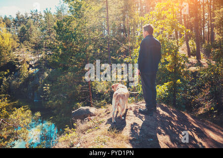 A man with Labrador retriever dog walking in the forest in autumn. Man and dog looking at the lake Stock Photo