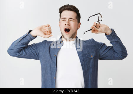 Portrait of tired attractive male student taking off glasses closing eyes and yawning while stretching as feeling exhausted and sleepy, working on project at night falling asleep dreaming about nap Stock Photo