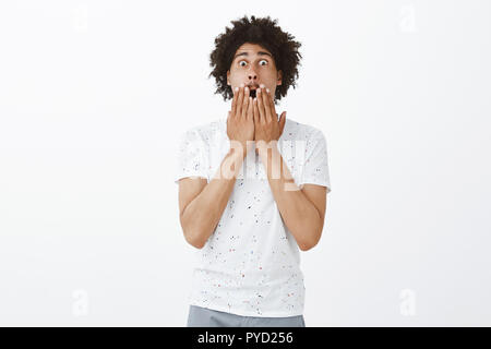 Portrait of emotive shocked and amazed good-looking man with moustache and afro hairstyle, dropping jaw from astonishment, covering opened mouth with palms and screaming from emotions Stock Photo