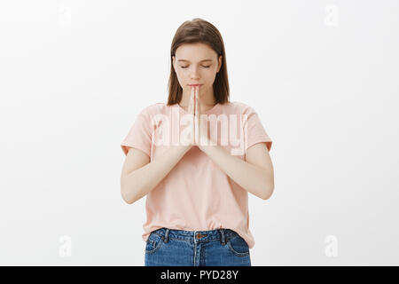 Girl praying for health and peace. Portrait of focused relaxed good-looking woman with short hair, closing eyes, holding hands in pray and tilting head down while talking to god or making wish Stock Photo