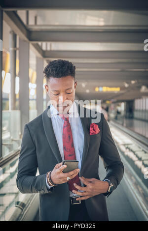 Close up of one young and attractive businessman going to the airport looking at his smartwatch to be on time. He is wearing a black suit with a red t Stock Photo