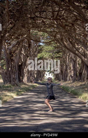 Caucasian female raises arms up at the Cypress Tree Tunnel on Point Reyes National Seashore in Marin County in Northern California Stock Photo