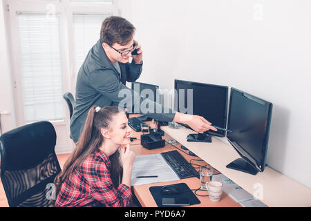 Image of happy young colleagues sitting in office, working on projekt and using desktop computers Stock Photo