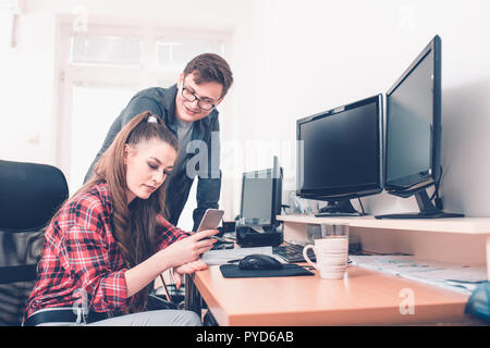Smiling young business colleagues using smartphone and talking in office Stock Photo