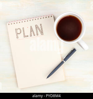 A photo of a spiral notepad with the word Plan, with a cup of coffee and a pen, shot from the top on a light wooden background with a place for text Stock Photo