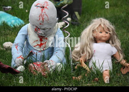 Pure evil zombie baby with a fork and a bloody mouth sitting next to a beautiful blond doll as creative Halloween lawn decorations. Stock Photo