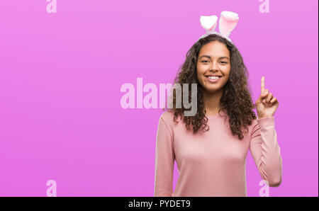 Young hispanic woman wearing easter bunny ears surprised with an idea or question pointing finger with happy face, number one Stock Photo