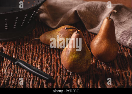 Still life scene of three pears, a paring knife, colander and towel on a woven twig background. Stock Photo