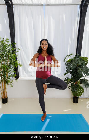 Smiling pregnant woman doing prenatal yoga in tree pose Stock Photo